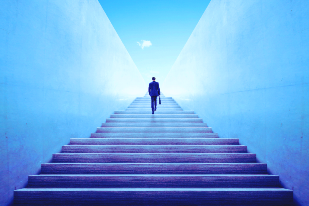 Man walking up a lot of stairs in business attire towards a bright light