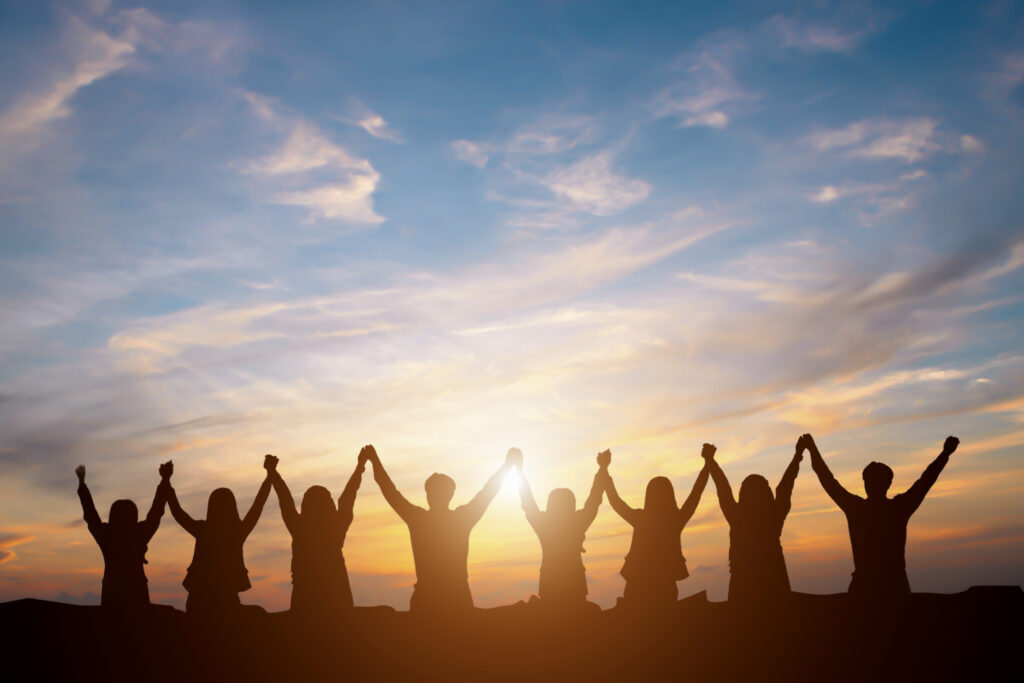 A group of people holding hands in the air with a sunset in the background